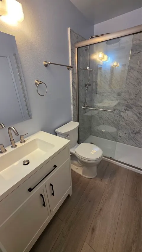 Bathroom finished with wood-look vinyl plank floor, white vanity and glass shower
