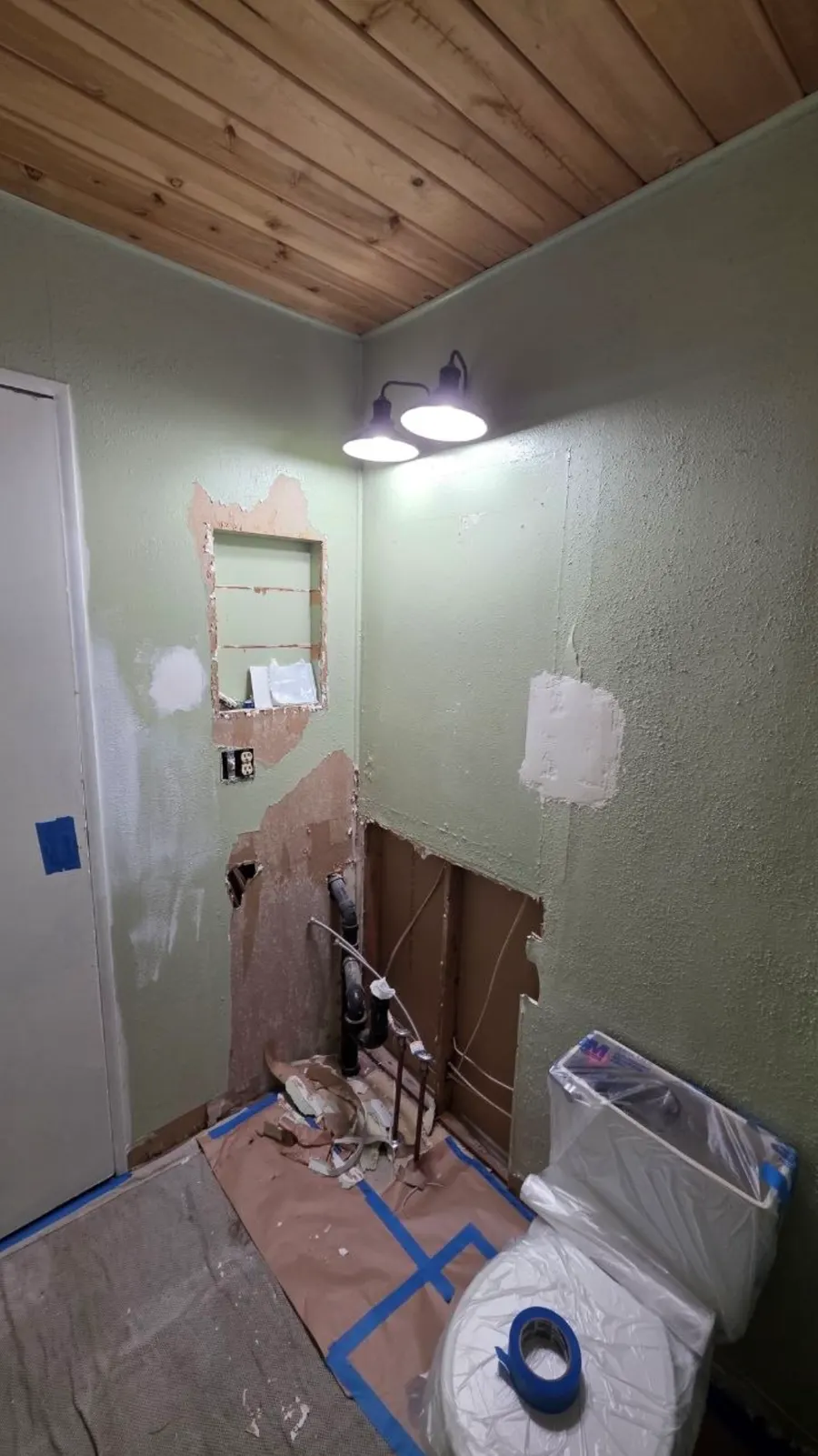 Bathroom wall opened up for plumbing, with torn drywall and an old medicine cabinet cut-out